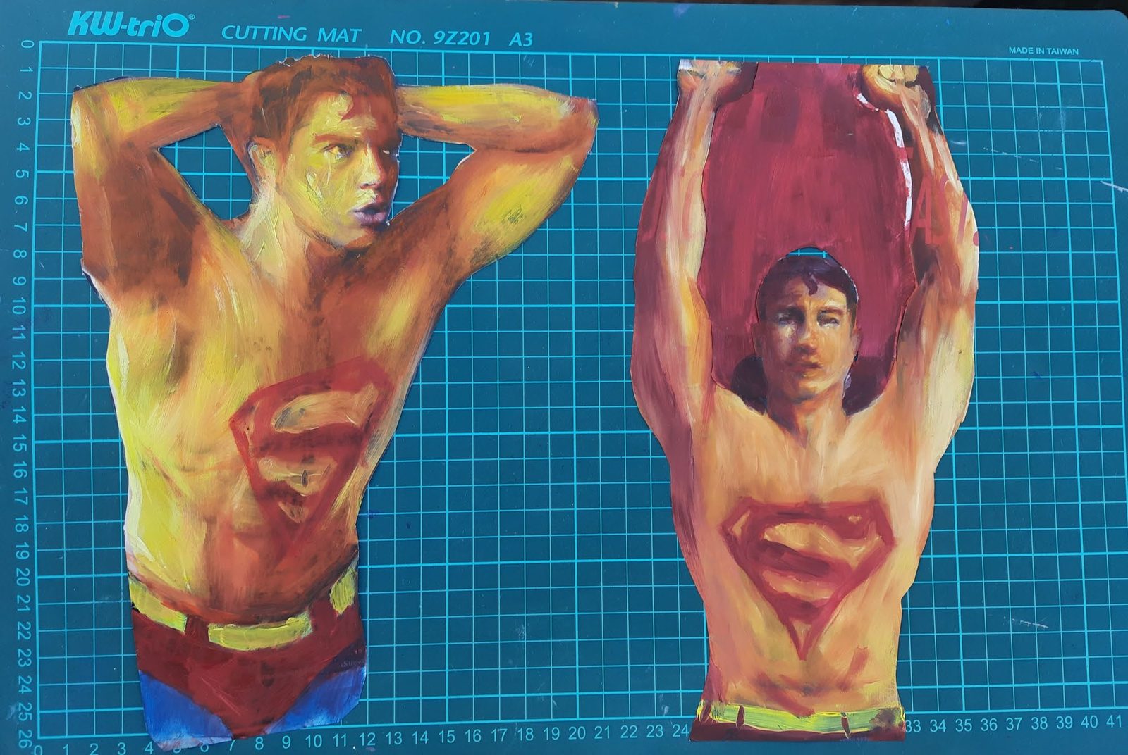 Two Paper Superman cutouts on a cutting mat