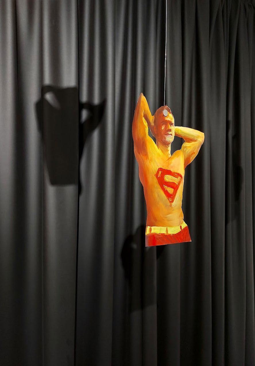 Paper Superman hanging on thread against a black curtain