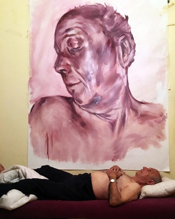 Jalal lying on a bed beneath a large painted portrait of himself